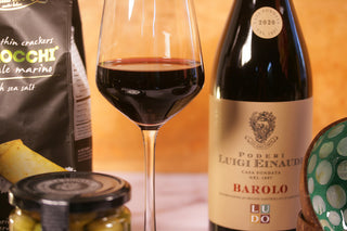 Luigi Einaudi Barolo wine bottle with a glass of red wine and snacks. Luxury Gift