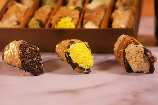 Three dessert canoli with different fillings on a light surface, with a blurred background of more canoli. Luxury Gifts